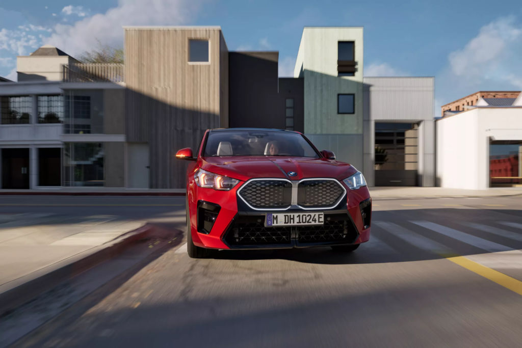 BMW iX2 rouge roulant dans une rue avec des habitations autour